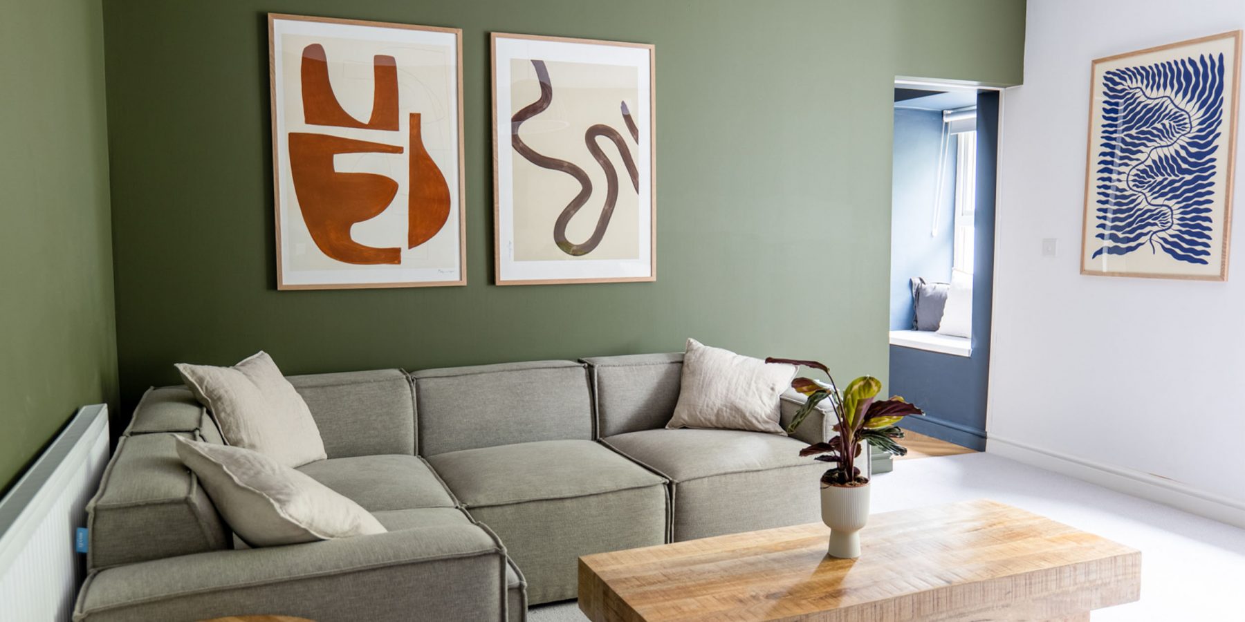 Living room, sofa, table, green walls, paintings, natural light